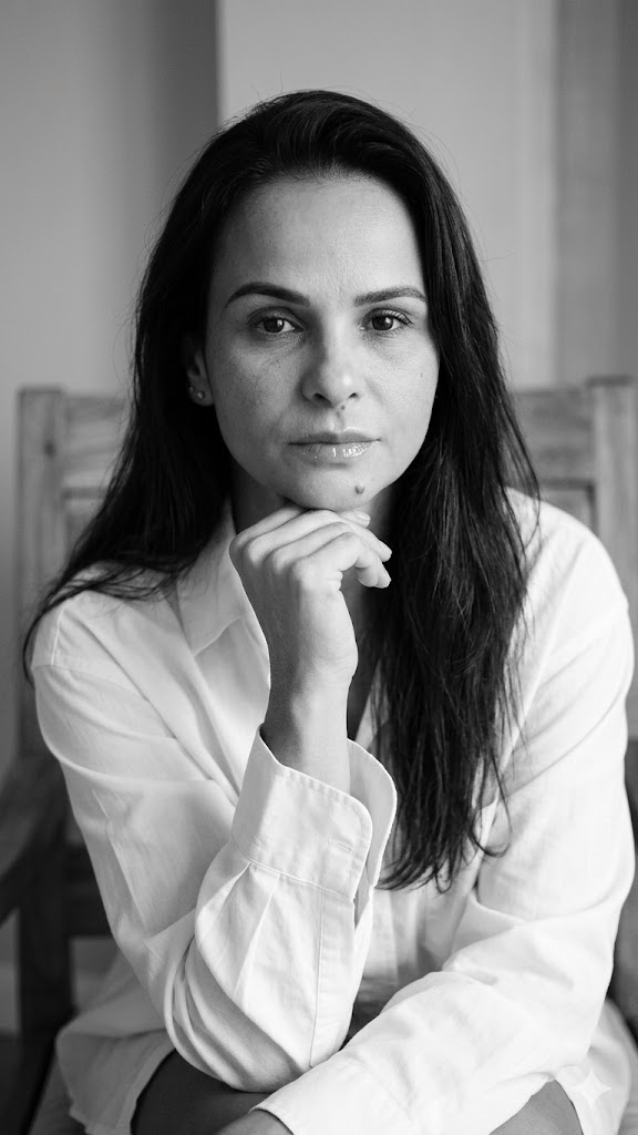 Cristina Moret, de camisa branca, sentada, olhando para a câmera